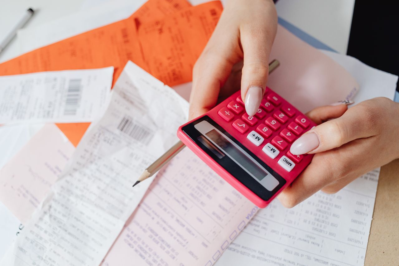 The Art of Drawing Readers In: Your attractive post title goes here Hands using a pink calculator to manage expenses amidst various receipts and documents.
