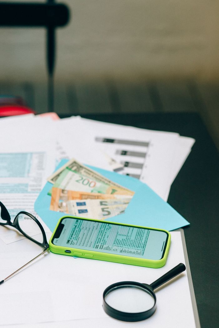 Mastering the First Impression: Your intriguing post title goes here Close-up of a desk with smartphone, financial documents, euro bills, and magnifying glass.